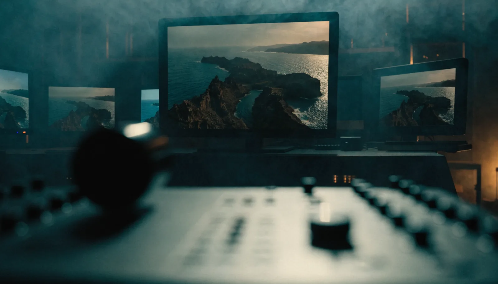 Sala de postproducción de cine de alta gama con monitores de referencia calibrados; una pantalla muestra una toma aérea de dron de un litoral.