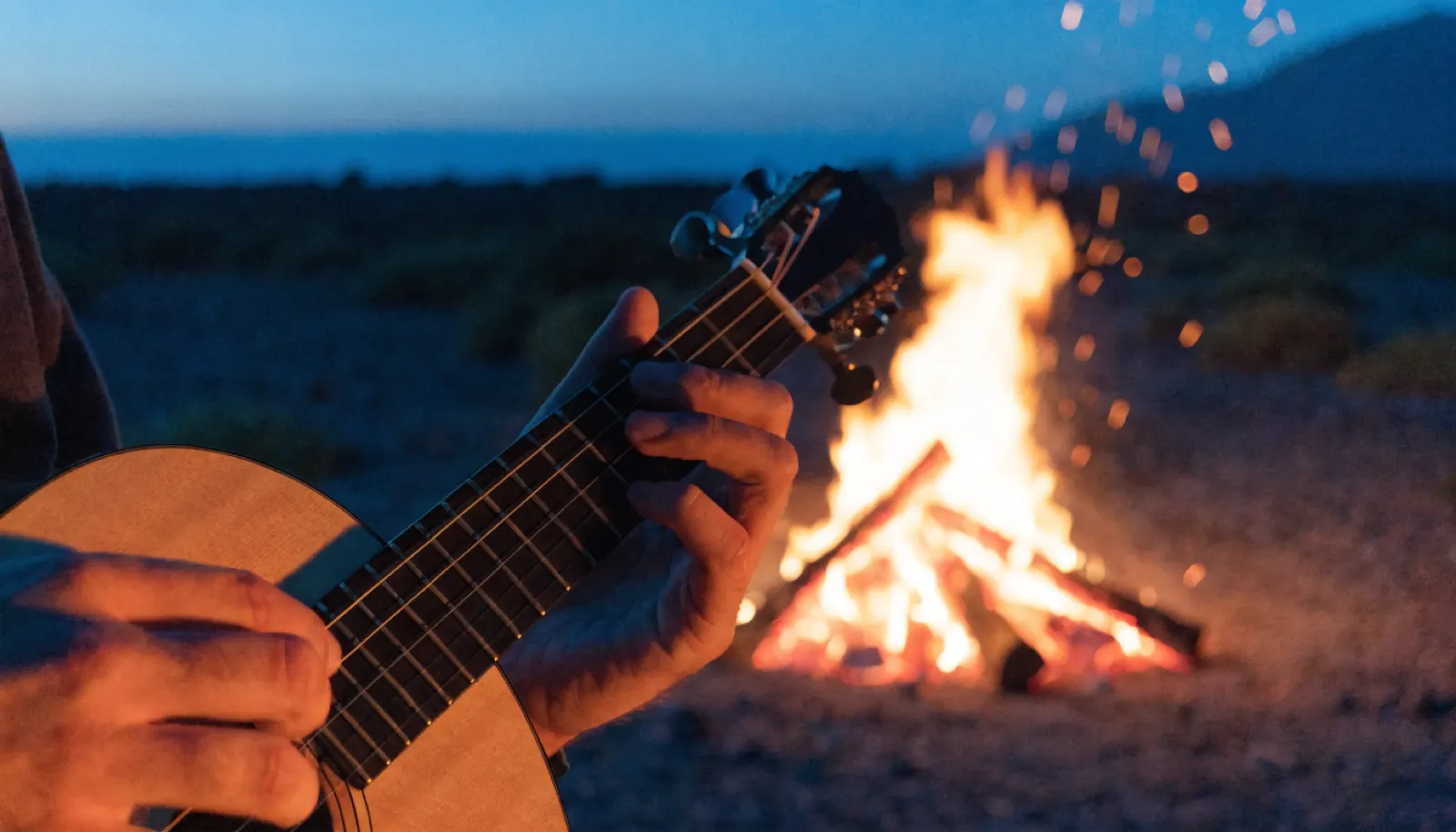 Manos tocando el timple junto a una hoguera nocturna, música canaria Mestisay