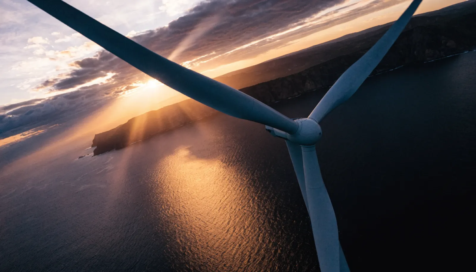 Aspas de aerogenerador en primer plano sobre el océano dorado, energía eólica en Canarias